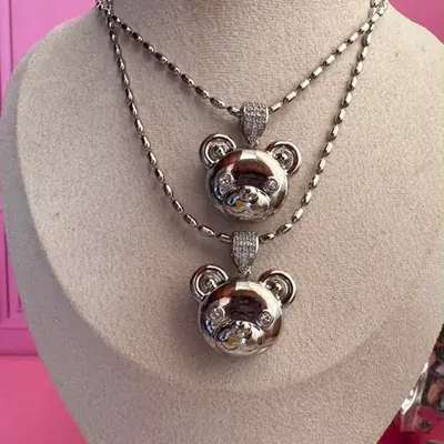 Dos collares plateados con dije de oso y circonias, en exhibidor beige