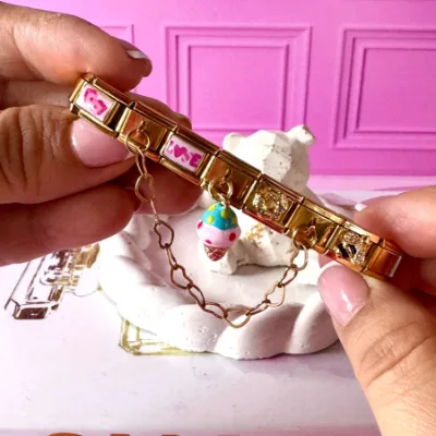 Pulsera en acero elástica color dorado. Dije de dados rosa, dije de cadena corazon, dije de love rosa, dije colgante de cono rosa, dije de dona, dije de cadena colgante corazon, dije de abeja. 6 charms