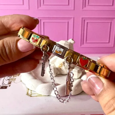 Pulso en acero elatisca en color dorado y dijes en combinaciones dorados y plateados. Dije de cereza, conejos fresa. Dije colgante de llave y candado color plateado. 5 dijes