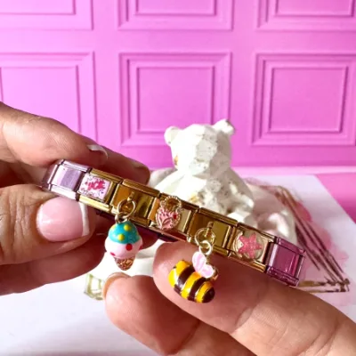 Pulsera en acero elástica pulso en color rosado y dijes color dorado de luck, dije colgante de helado, dije de candado, dije colgante de abeja y dije de estrella de mar. 5 dijes
