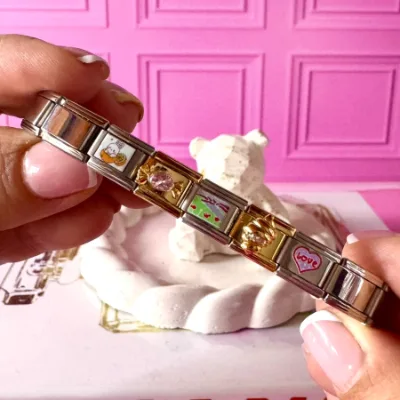 Pulsera en acero elástica, pulso en color plateado dijes en plateado y dorado. Dije de conejo, caramelo con cristal rosado, dije de paisaje, dije de cono, dije de corazon love. 5 charms